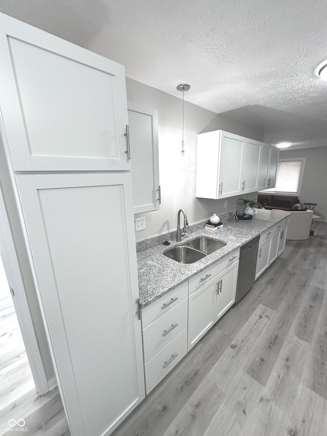 kitchen featuring light wood finished floors, white cabinets, a sink, a textured ceiling, and stainless steel dishwasher