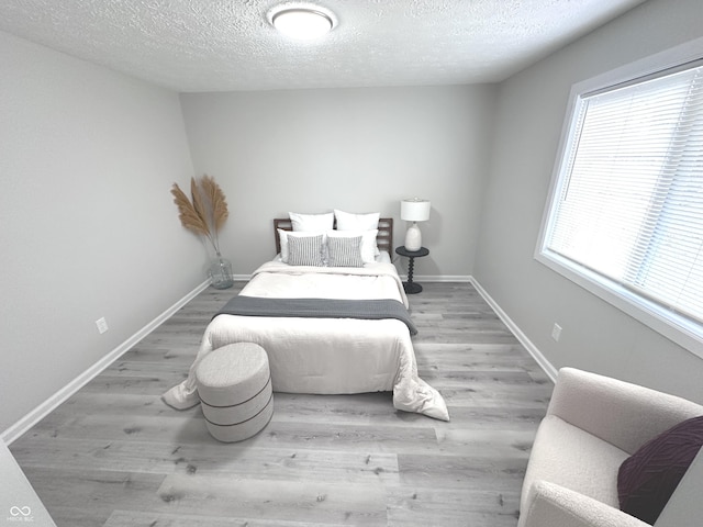 bedroom featuring a textured ceiling, baseboards, and wood finished floors