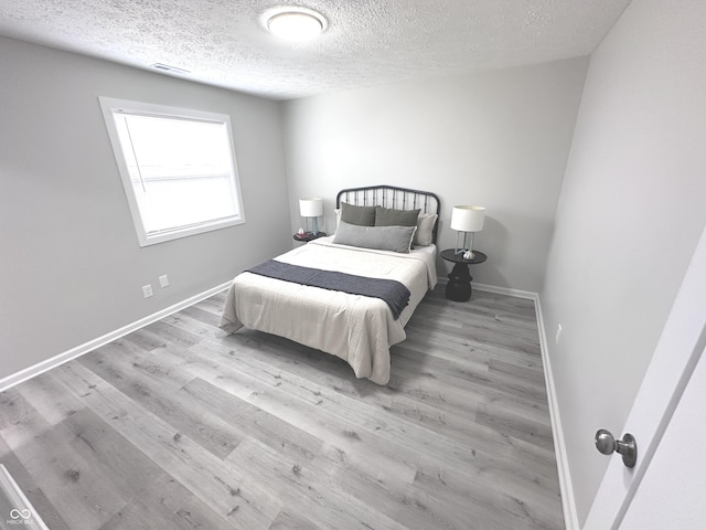 bedroom with visible vents, a textured ceiling, baseboards, and wood finished floors