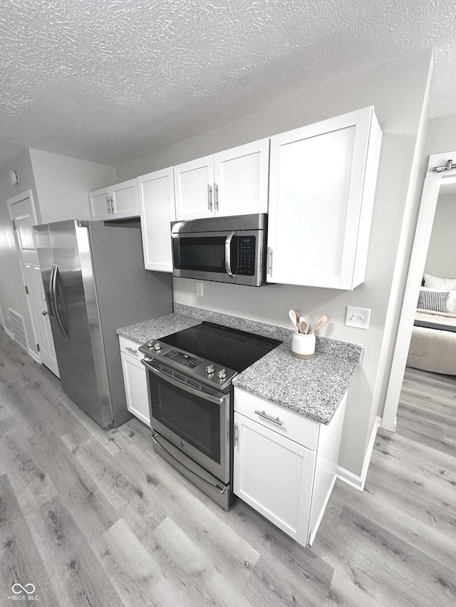 kitchen with light stone countertops, light wood finished floors, white cabinetry, and appliances with stainless steel finishes