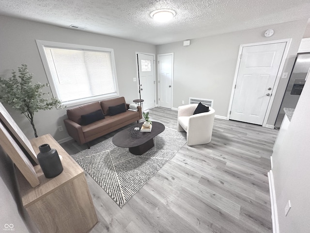 living area with a textured ceiling, wood finished floors, visible vents, and baseboards