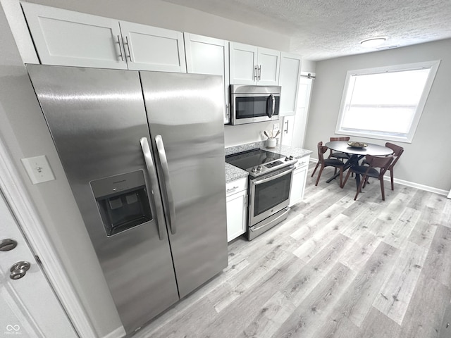 kitchen with light wood-type flooring, white cabinetry, stainless steel appliances, and a textured ceiling