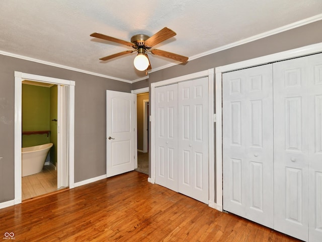 unfurnished bedroom with light wood finished floors, crown molding, baseboards, and two closets