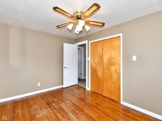 unfurnished bedroom featuring a closet, a textured ceiling, baseboards, and hardwood / wood-style floors