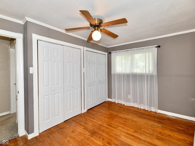 unfurnished bedroom with crown molding, two closets, a ceiling fan, wood finished floors, and baseboards