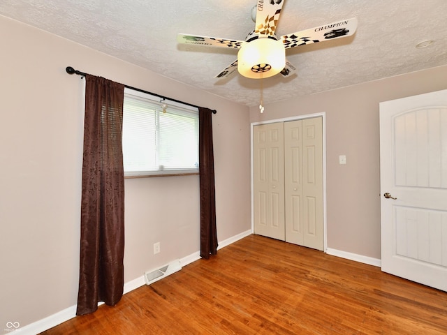 unfurnished bedroom with baseboards, a textured ceiling, visible vents, and wood finished floors