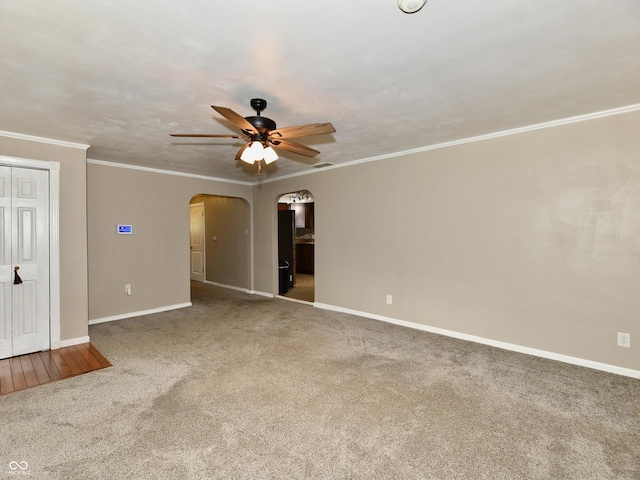 carpeted spare room featuring baseboards, ceiling fan, arched walkways, and crown molding