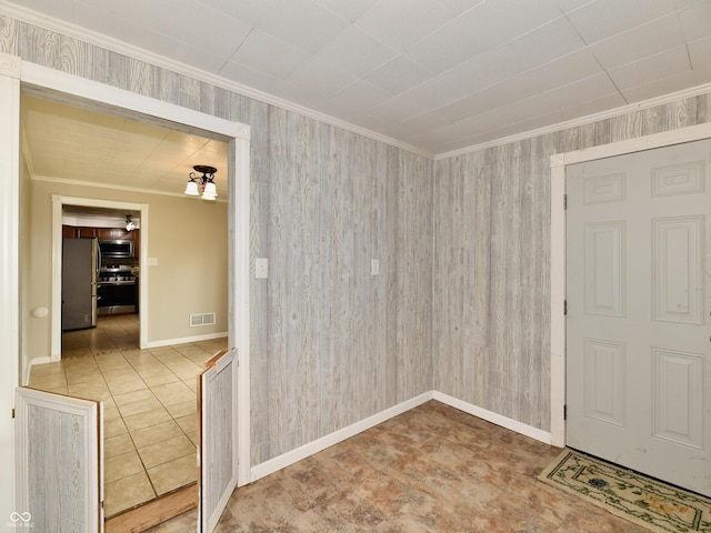 spare room with wood walls, baseboards, visible vents, and crown molding