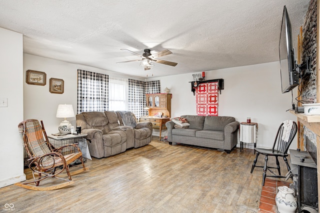 living area with a textured ceiling, a fireplace, a ceiling fan, and wood finished floors