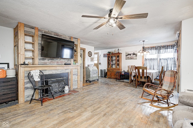 living room with a textured ceiling, a stone fireplace, wood finished floors, and ceiling fan with notable chandelier