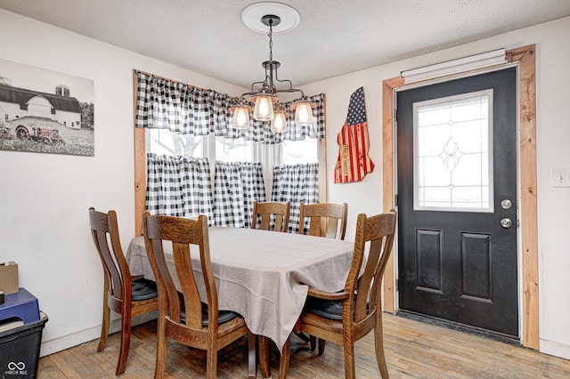 dining room featuring light wood-type flooring, baseboards, a chandelier, and a textured ceiling