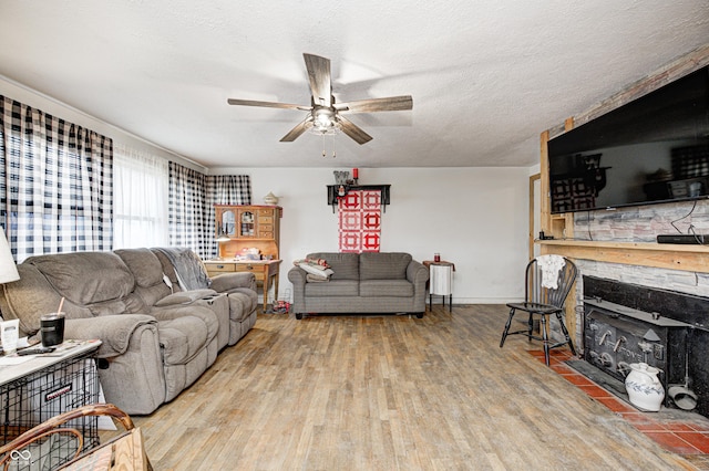 living area featuring baseboards, a ceiling fan, wood finished floors, a textured ceiling, and a fireplace