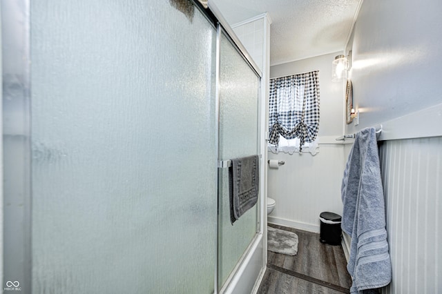 full bathroom featuring toilet, a textured ceiling, wood finished floors, and a shower with shower door