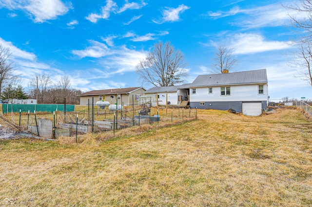 rear view of house featuring a yard, a vegetable garden, a chimney, metal roof, and fence