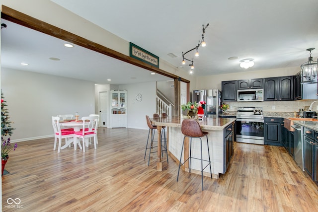 kitchen with light wood-style flooring, a kitchen bar, appliances with stainless steel finishes, and decorative backsplash