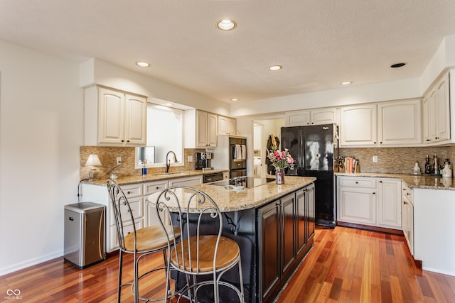 kitchen with a kitchen bar, black appliances, a sink, a kitchen island, and wood finished floors