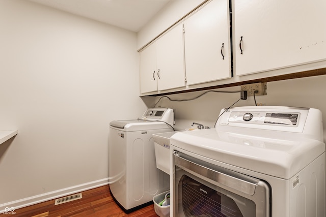 washroom with wood finished floors, baseboards, visible vents, cabinet space, and washing machine and dryer