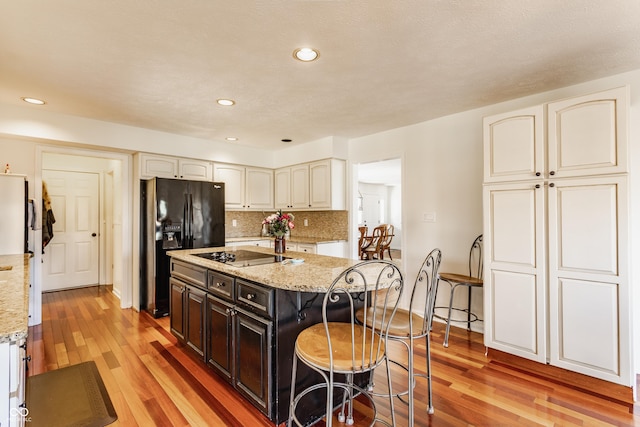 kitchen featuring black appliances, light stone counters, a kitchen breakfast bar, light wood-style floors, and decorative backsplash