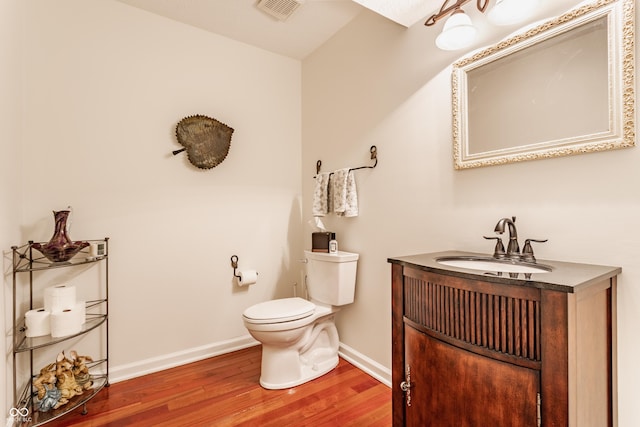 half bathroom with visible vents, baseboards, toilet, wood finished floors, and vanity