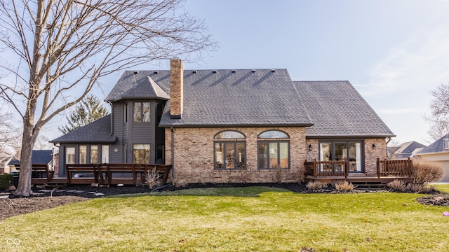 rear view of property with brick siding, a lawn, a deck, and roof with shingles