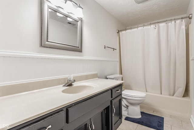 bathroom featuring a wainscoted wall, toilet, shower / tub combo with curtain, a textured ceiling, and vanity