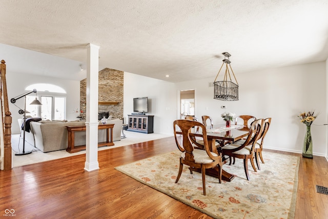 dining area with a textured ceiling, wood finished floors, a stone fireplace, baseboards, and vaulted ceiling