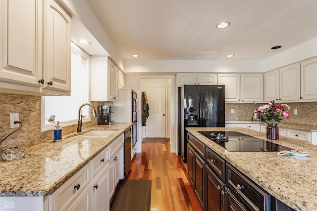 kitchen with light stone counters, light wood-style flooring, black appliances, and a sink