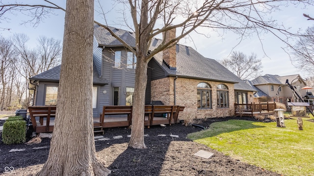 rear view of property featuring a lawn, a chimney, a deck, and a shingled roof