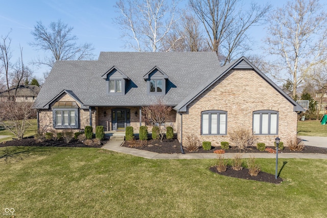 view of front facade featuring brick siding, covered porch, a front yard, and a shingled roof