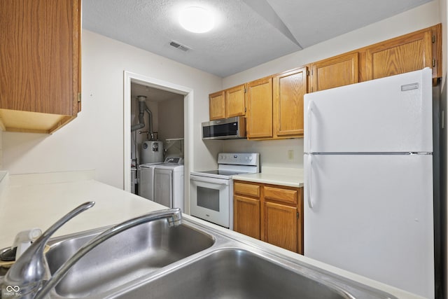 kitchen with a textured ceiling, white appliances, visible vents, light countertops, and washer and clothes dryer