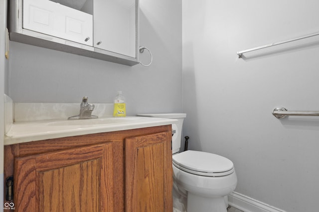 half bathroom featuring toilet, baseboards, and vanity