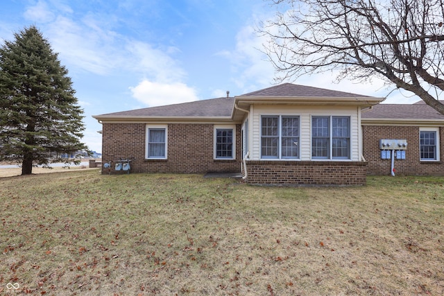 rear view of house with roof with shingles, a lawn, and brick siding