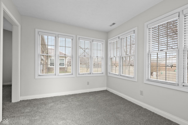 empty room with baseboards, visible vents, and dark colored carpet