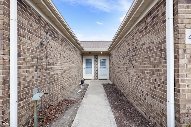 doorway to property featuring brick siding and roof with shingles