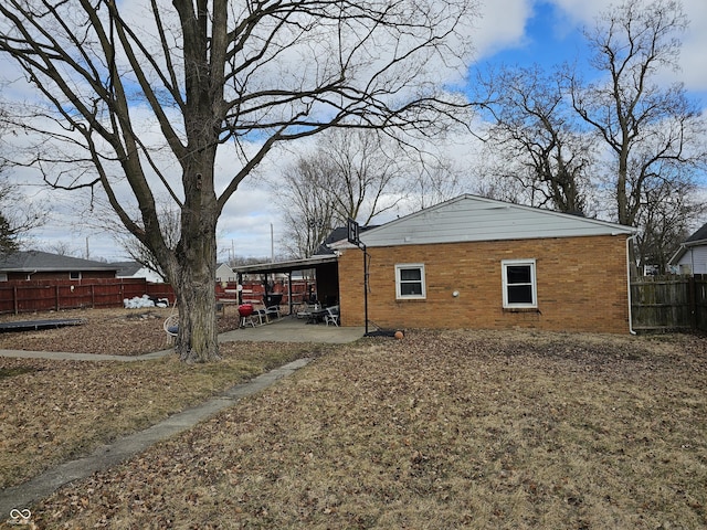 view of side of property featuring brick siding, a patio area, and fence