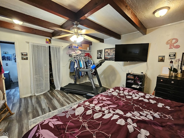 bedroom featuring beam ceiling, ceiling fan, a textured ceiling, wood finished floors, and baseboards