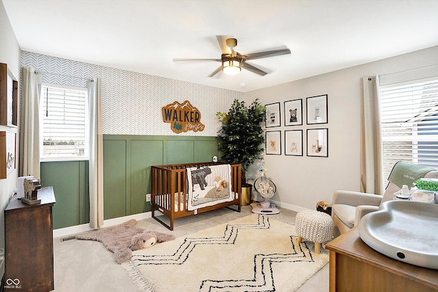 carpeted bedroom featuring wallpapered walls, baseboards, ceiling fan, an accent wall, and a nursery area