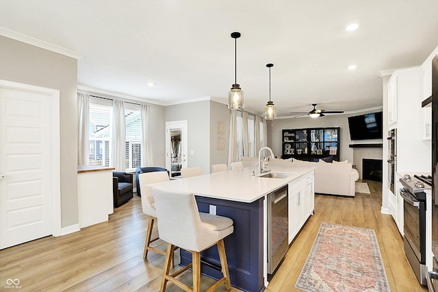 kitchen featuring light wood finished floors, gas range, open floor plan, crown molding, and a sink