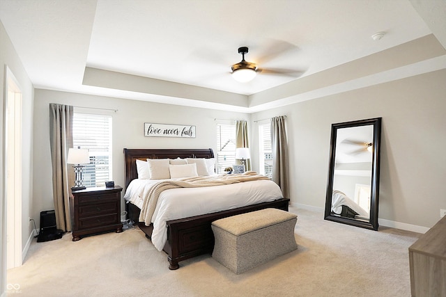 bedroom with baseboards, a tray ceiling, multiple windows, and light colored carpet