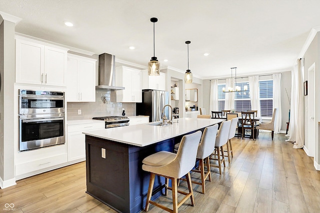 kitchen featuring a large island, light wood finished floors, light countertops, appliances with stainless steel finishes, and wall chimney range hood