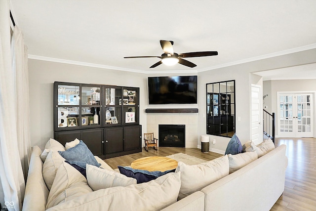 living room featuring a fireplace, wood finished floors, a ceiling fan, ornamental molding, and french doors