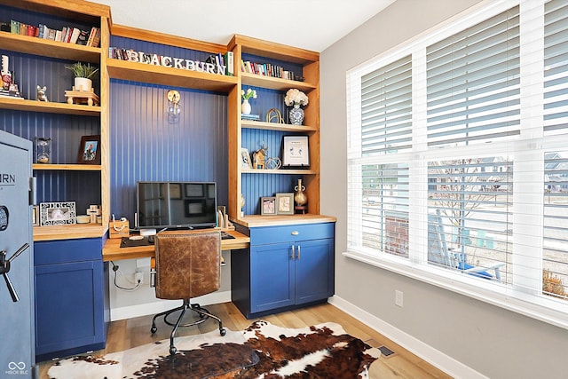 office area with light wood-style flooring, visible vents, baseboards, and built in desk