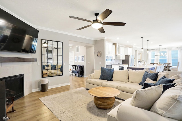 living room with crown molding, visible vents, a tiled fireplace, light wood-type flooring, and baseboards