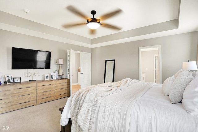 bedroom featuring light carpet, a tray ceiling, a ceiling fan, and ensuite bathroom