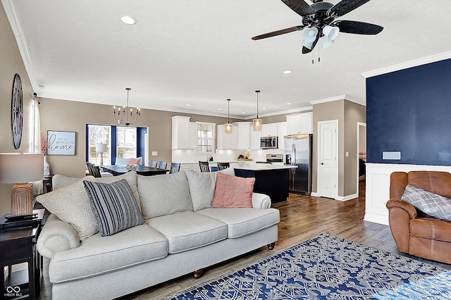 living room featuring ornamental molding, recessed lighting, dark wood-style flooring, and ceiling fan with notable chandelier