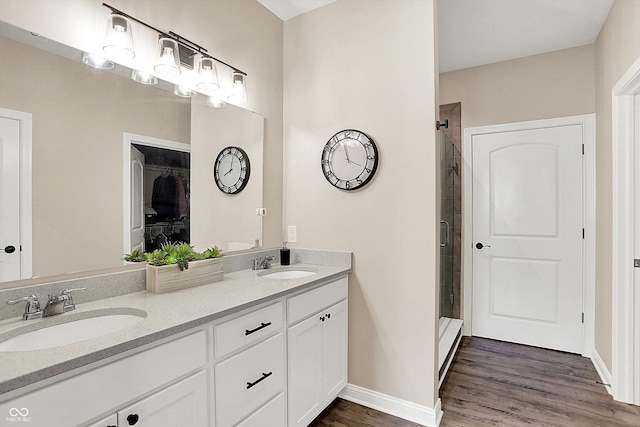 full bath with double vanity, a sink, a shower stall, and wood finished floors