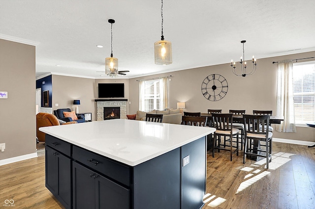 kitchen featuring a fireplace, light wood finished floors, light countertops, hanging light fixtures, and ornamental molding