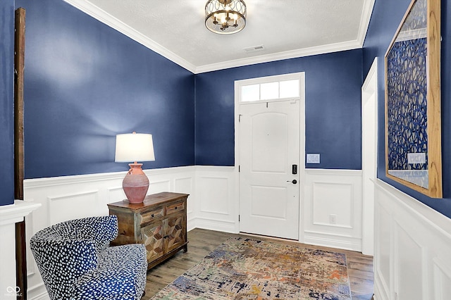 entryway with a wainscoted wall, a notable chandelier, visible vents, ornamental molding, and wood finished floors