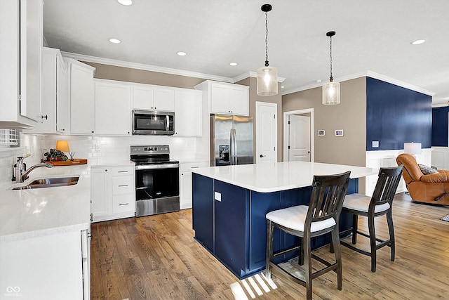 kitchen with stainless steel appliances, light countertops, a kitchen island, a sink, and wood finished floors