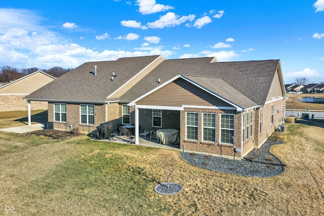 back of house with a yard, a patio, brick siding, and a shingled roof